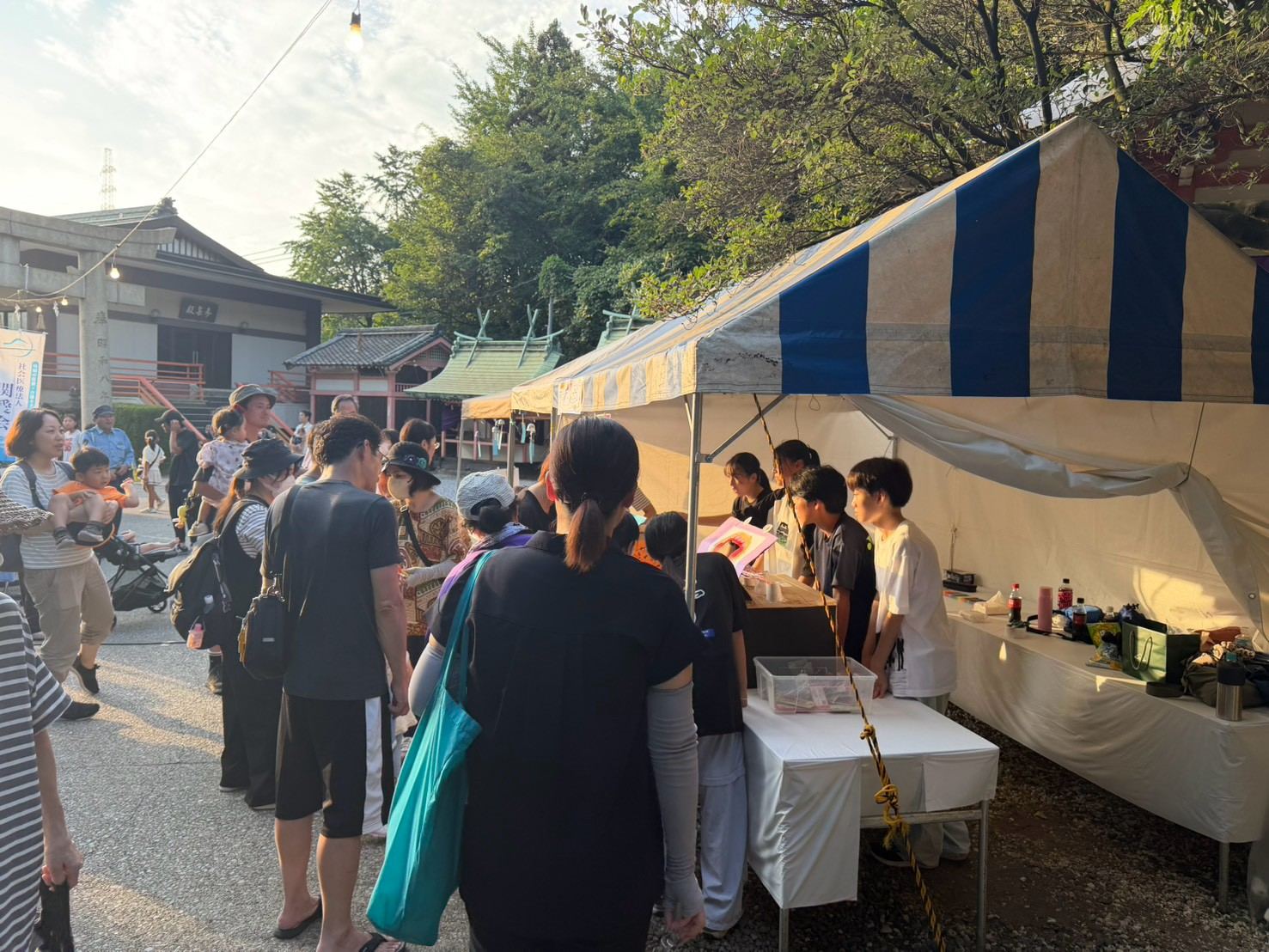 神社の境内に立てた青と白の天幕の下で、並んだお客さんに応対する子どもたち